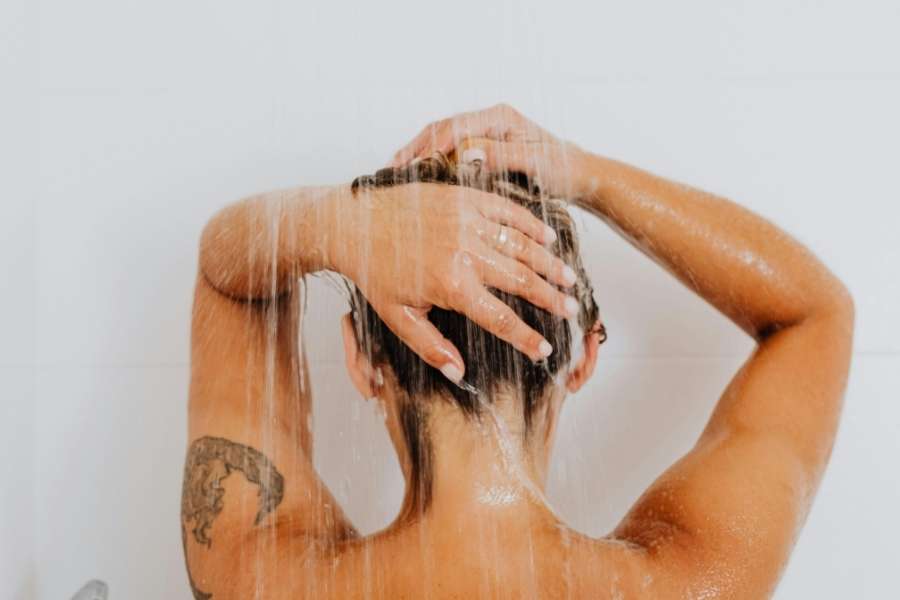 Personne se lavant les cheveux sous la douche avec eau ruisselante, entretenir sa douche efficacement