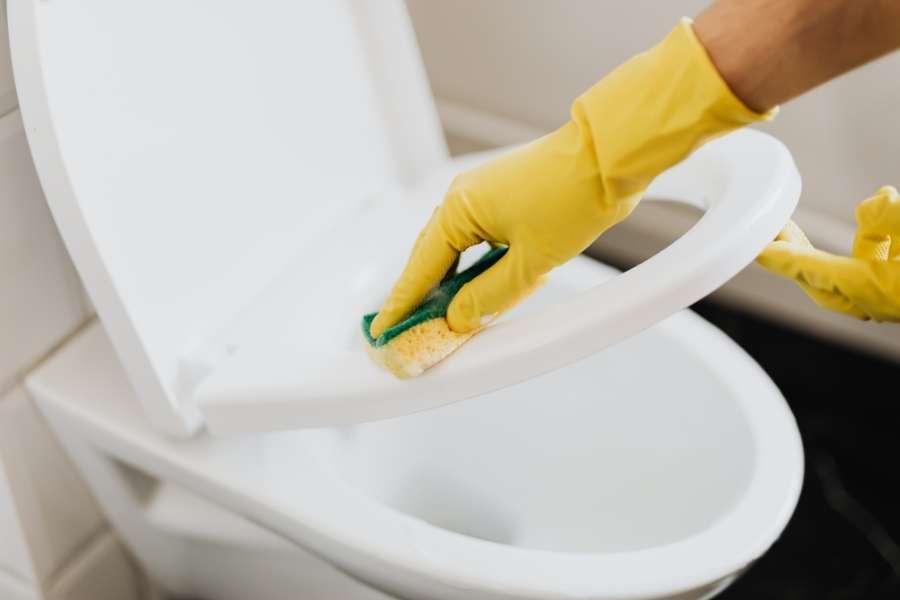 Mains gantées de jaune nettoyant l'abattant d'un WC japonais avec une éponge verte