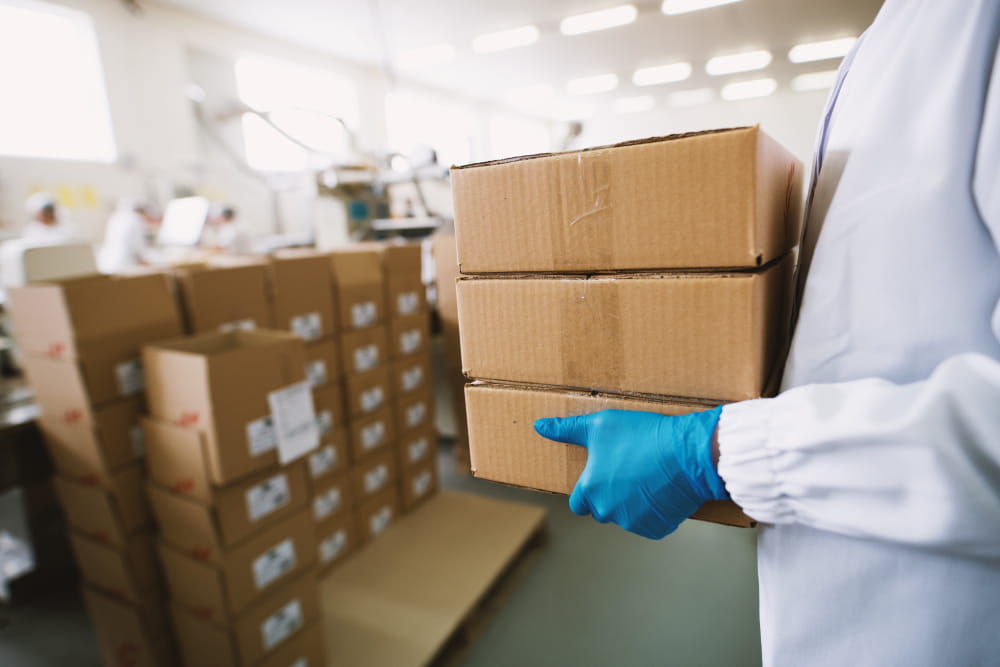 Un technicien en blouse blanche et gants de protection manipule des cartons lors d'un déménagement de laboratoire