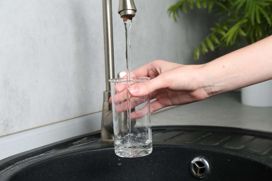Une main tient un béreau gradué sous un robinet de cuisine, recueillant de l'eau claire pour analyser si l'eau de votre robinet sent le fer.